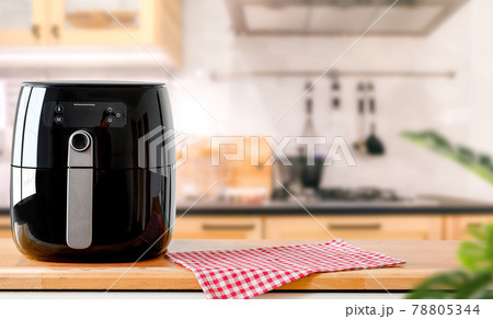 An electric Air Fryer on table with blurred kitchen background. Lifestyle of new normal cooking. An electric Air Fryer on table with blurred kitchen background. Lifestyle of new normal cooking. 78805344