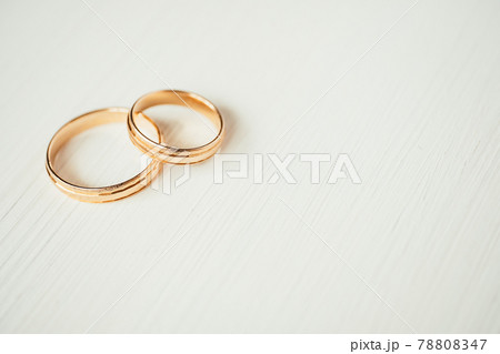 Intersecting wedding gold rings in the left part of white wooden background. Side view. 78808347