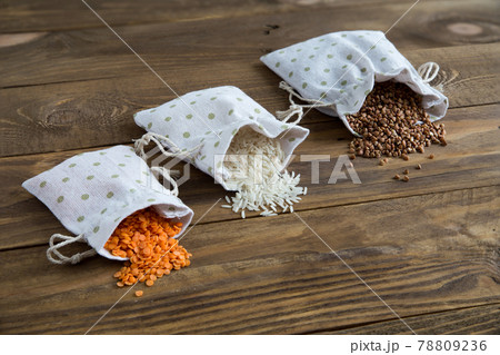 Three types of cereals buckwheat, rice and lentils in canvas bags. They lie on wooden background. Grains are scattered on table. Organic healthy cereals. Natural vegetarian vegetable protein. Close up Three types of cereals buckwheat, rice and lentils in canvas bags. They lie on wooden background. Grains are scattered on table. Organic healthy cereals. Natural vegetarian vegetable protein. Close up 78809236