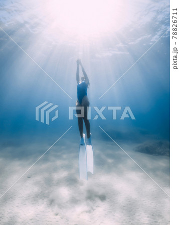 Female freediver glides with fins underwater in ocean with sunlight. 78826711