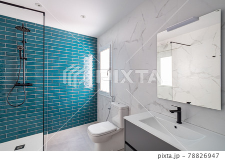 Decorated with dark aquamarine and white colors. Modern tiled bathroom with shower zone, new sink and toilet. 78826947