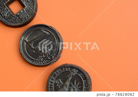 Three chocolate products in the form of Euro, USA and Japan coins lie on an orange plastic background. A model of cash coins in an edible form 78828082