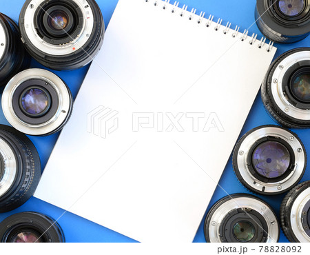 Several photographic lenses and white notebook lie on a bright blue background. Space for text Several photographic lenses and white notebook lie on a bright blue background. Space for text 78828092