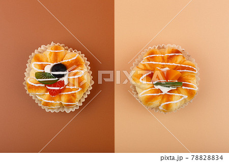 Top view of two cupcakes with pieces of peaches and kiwi fruit and cream on brown and beige background 78828834