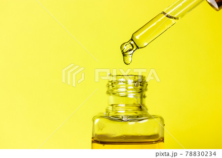 A drop of tanning oil on a tip of the dropper on yellow background. Cuticle Oil. 78830234