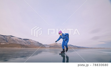 The child train on ice professional speed skating. The girl skates in the winter in sportswear, sport glasses, suit. Outdoor slow motion. 78830680