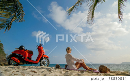 Scooter road trip. Woman alone on red motorbike in white clothes on sand beach by ocean. One girl caucasian tourist walk near tropical palm tree. 78830814