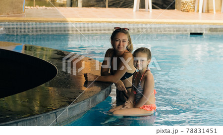 The pretty woman drinking blue cocktail alcohol liquor and sit at the bar. Cocktail bar in the swimming pool. Portrait of sexy girl in pool outdoor. 78831451