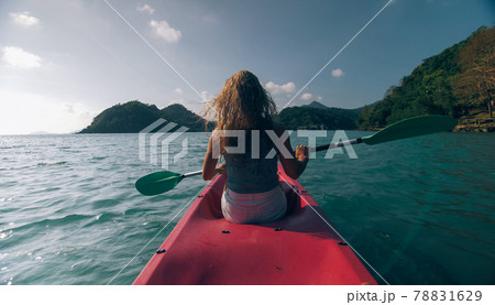 Silhouette of woman tourist raising hands while sailing in canoe along sea bay water to distant hilly island backside view. Silhouette of woman tourist raising hands while sailing in canoe along sea bay water to distant hilly island backside view. 78831629