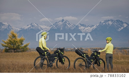 The man and woman travel on mixed terrain cycle touring with bikepacking. The two people journey with bicycle bags. Mountain snow capped. The man and woman travel on mixed terrain cycle touring with bikepacking. The two people journey with bicycle bags. Mountain snow capped. 78833102