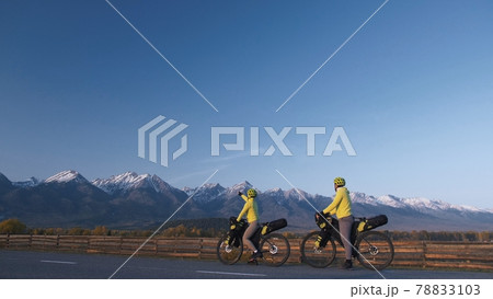 The man and woman travel on mixed terrain cycle touring with bikepacking. The couple journey with bicycle bags. Mountain snow capped. 78833103