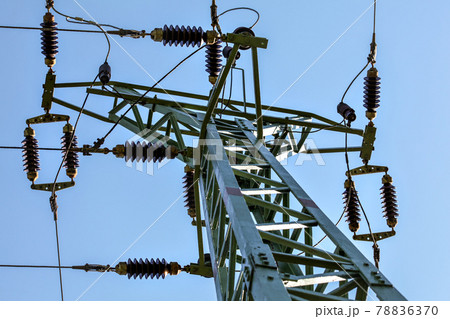 View from ground to power pylon top. Cables and ceramic isolators visible against blue sky. Abstract power industry background. View from ground to power pylon top. Cables and ceramic isolators visible against blue sky. Abstract power industry background. 78836370