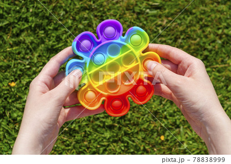 Hands press rubber pimples of pimpled anti stress pop it toy on green lawn 78838999