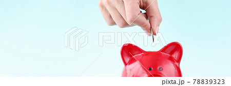 Womans hand throwing coin into red piggy bank closeup Womans hand throwing coin into red piggy bank closeup 78839323