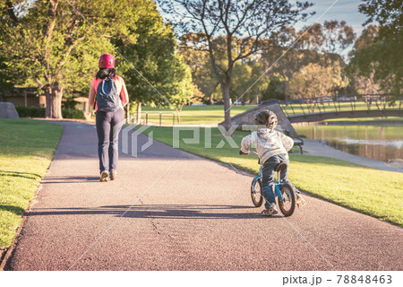 Litle boy riding his balance bike while following his mother Litle boy riding his balance bike while following his mother 78848463