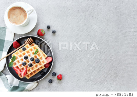 Waffles plate on table with blueberry, strawberry, mint and white cup of coffee 78851583