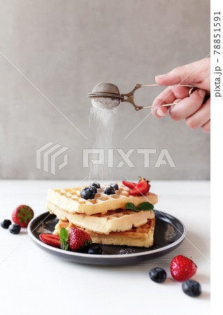 Hand is shaking powdered sugar over stack of waffles with blueberry, strawberry Hand is shaking powdered sugar over stack of waffles with blueberry, strawberry 78851591