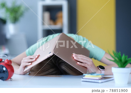 Tired in stress woman hides her head with laptop at workplace. 78851900