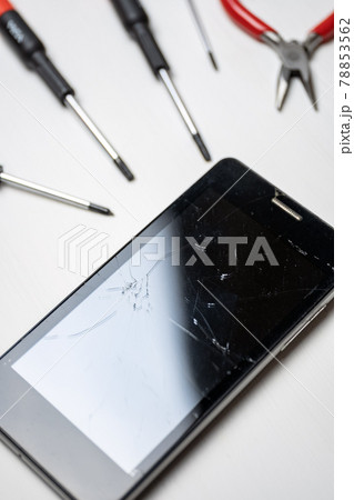 Smartphone with broken and cracked screen with screwdrivers and pliers on white background. Vertical. Smartphone with broken and cracked screen with screwdrivers and pliers on white background. Vertical. 78853562
