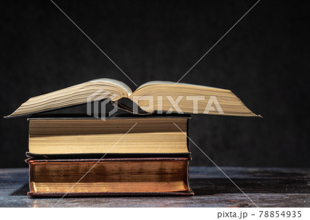 A stack of old books lying on a table on a dark background A stack of old books lying on a table on a dark background 78854935