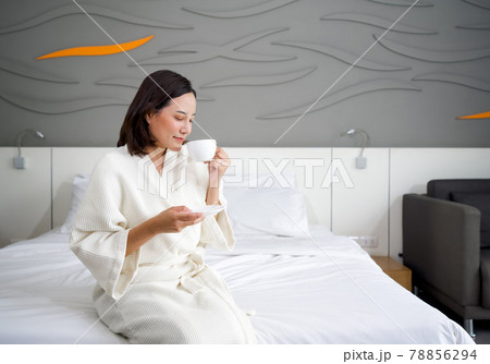 Asian woman in a bathrobe drinking hot coffee on bed in the morning. 78856294