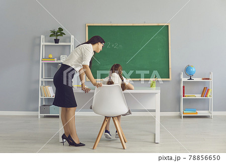 Teacher standing and checking girl pupil sitting and doing homework in school 78856650