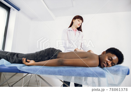 young woman physiotherapist make neck and shoulder massage for African American male patient 78861378