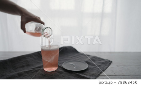 Man pour pink sparkling drink into tumbler glass with ice chunk 78863450