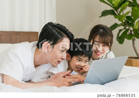 寝室のベッドで寝転がりながらノートパソコンを見る3人家族 78866535