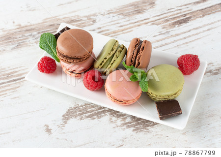 Variety of french macaroons with raspberry, blueberry, mint leaf and chocolate on a plate over wooden background. Variety of french macaroons with raspberry, blueberry, mint leaf and chocolate on a plate over wooden background. 78867799