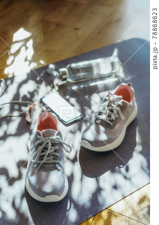 Bottle with water, smartphone, earphones and sneakers on the mat background with direct sunlight and shadows. Set for running and sports activities . Fitness, healthy and active lifestyle. Vertical. 78868623