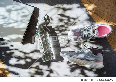 Laptop, sneakers and water bottle on a gray yoga mat background with direct sunlight and shadows. Online Fitness program, Home workout. Workout essentials. Top view, flat lay 78868625