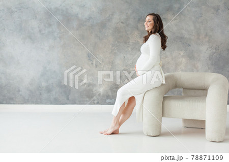 Cute pregnant woman resting on white armchair on gray banner background Cute pregnant woman resting on white armchair on gray banner background 78871109