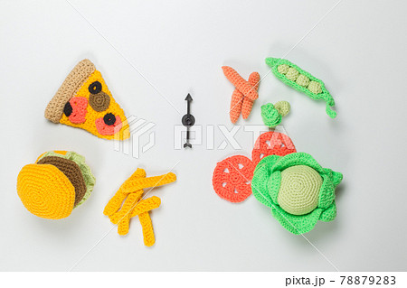 Children's toy knitted food. Pizza, hamburger and French fries on one side and vegetables on the other. Top view on a light background 78879283