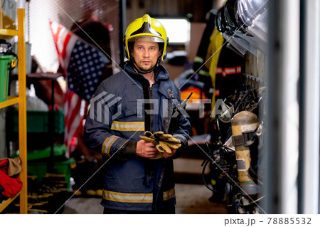 Fireman or firefighter man stand and hold the glove and look at camera also stay in room with tools Fireman or firefighter man stand and hold the glove and look at camera also stay in room with tools 78885532