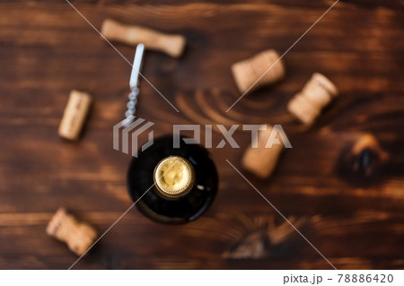A dark bottle of wine next to blurry a corkscrew and a twisted cork on a wooden background. A dark bottle of wine next to blurry a corkscrew and a twisted cork on a wooden background. 78886420