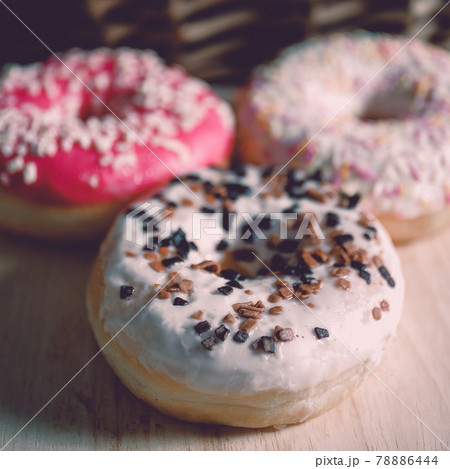 White, pink and brown glazed donuts on wooden background and near rattan basket . 78886444