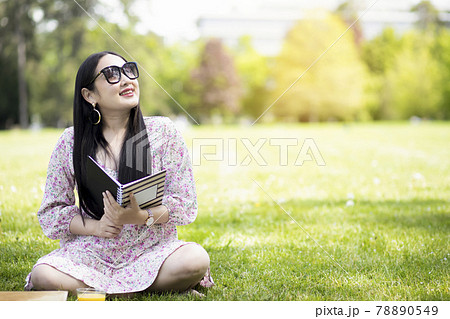 Working outside in summer or spring and WFH concept, Young beautiful Asian woman reading a book and looking laptop in the natural park, Freelance working, homeschooling, distance learning. 78890549