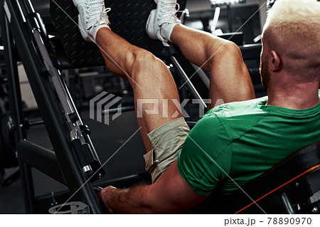 A man, a bodybuilder does exercises on his legs. The athlete trains his legs in the gym in the simulator. 78890970