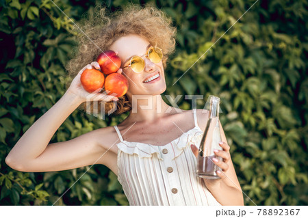 Curly-gaired young woman with nectarines looking happy 78892367