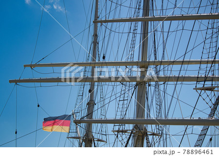 rigging and masts of a big sailing ship in front of a blue sky with the black-red-golden flag of the state Germany, ship 78896461