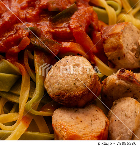 Crispy bite-sized pieces of German bratwurst with green and yellow ribbon noodles with mashed vegetables in tomato sauce, food 78896536