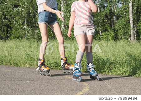 teenager girl and her little sister rollerskating in the park. partial view. sport and leisure concept. preshcool girl and teen spending time together teenager girl and her little sister rollerskating in the park. partial view. sport and leisure concept. preshcool girl and teen spending time together 78899484