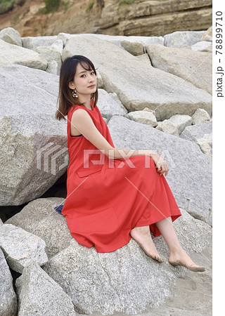 岩山に座り微笑む赤いワンピースを着た若い女性の写真素材 [78899710 ...