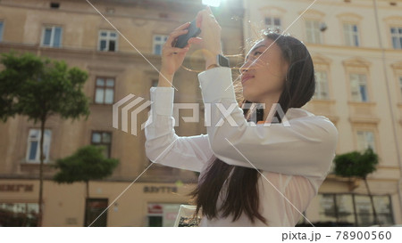Young asian woman using smartphone in the city, taking pictures. Girl makes a photo on the streets of the old town on a summer sunny day. Girl using cell phone photography app. Young asian woman using smartphone in the city, taking pictures. Girl makes a photo on the streets of the old town on a summer sunny day. Girl using cell phone photography app. 78900560