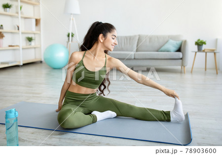 Young Indian lady stretching on yoga mat, making domestic workout, doing flexibility exercises at home 78903600