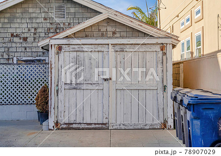 Trash bins in front of old shed with pitched roof and wooden door against homes Trash bins in front of old shed with pitched roof and wooden door against homes 78907029