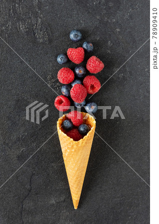 Mix of blueberry and raspberry berries in a waffle ice cream cone on black background top view. Mix of blueberry and raspberry berries in a waffle ice cream cone on black background top view. 78909410