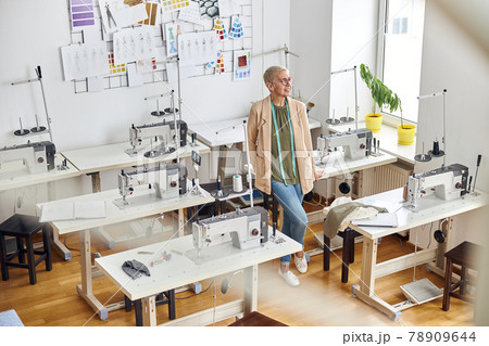 Female entrepreneur with tape measure leans onto table in empty sewing workshop Female entrepreneur with tape measure leans onto table in empty sewing workshop 78909644