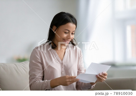 Happy young mixed race woman holding and reading paper letter Happy young mixed race woman holding and reading paper letter 78910030